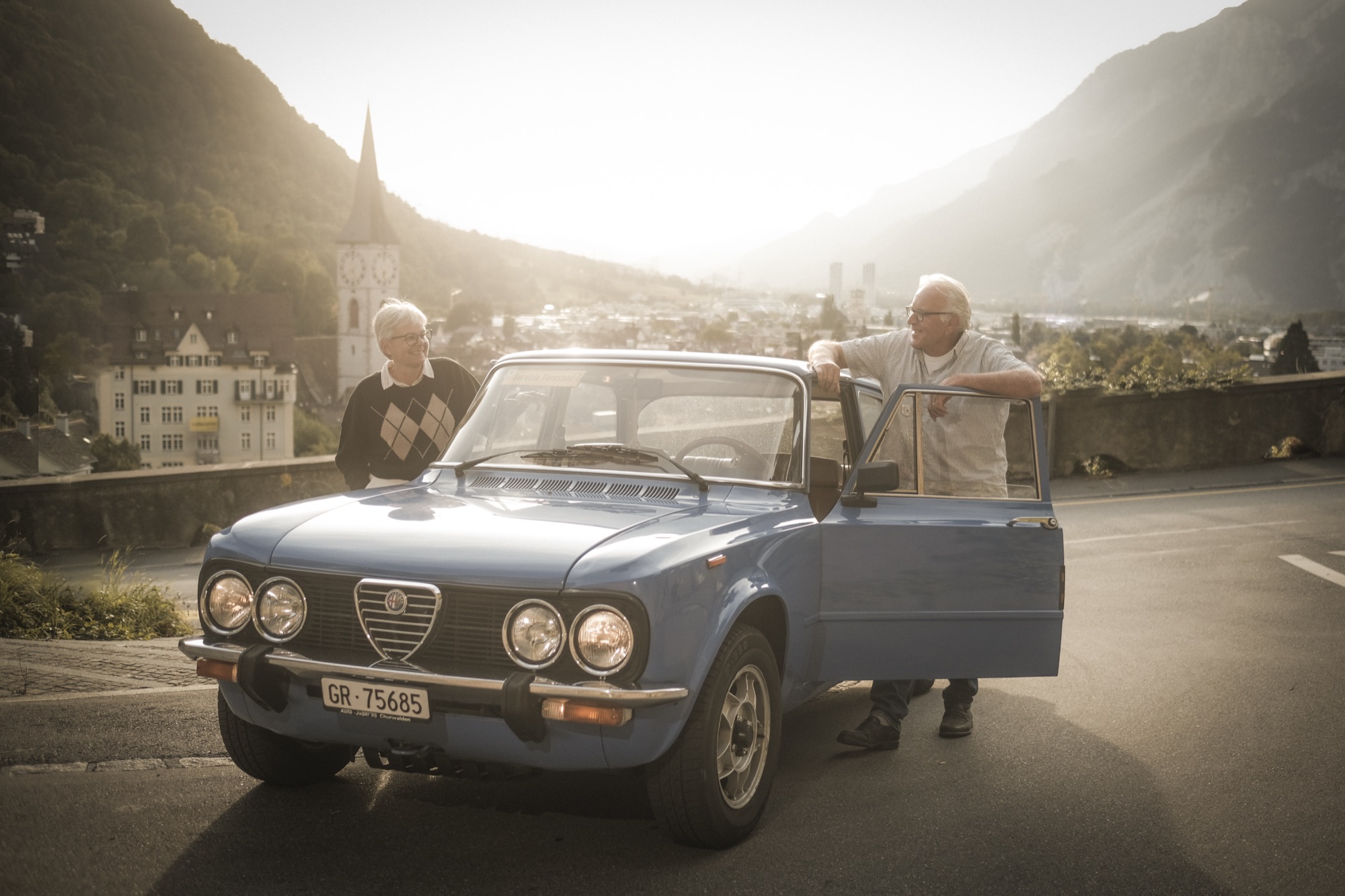 Ehepaar mit ihrem Alfa Romeo Giulia auf einer Passstrasse über Chur, Graubünden, Abendlicht