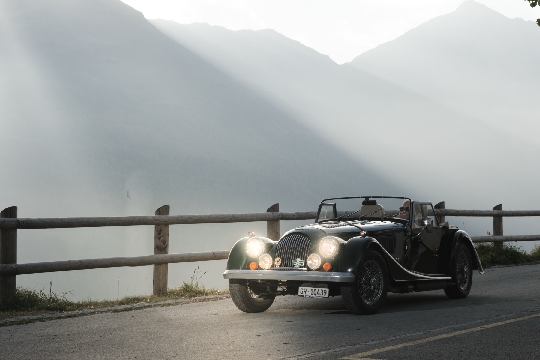 Autofotografie Morgan Roadster, Fahrer mit Pfeife, Blick ins Tal, Graubünden